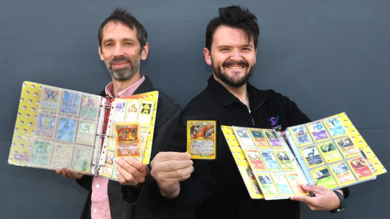 Hai nhân viên nhà đấu giá Ewbank's cầm album thẻ Pokémon và lá Charizard