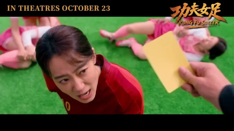 Cầu thủ áo đỏ nhăn mặt trước tấm thẻ vàng, phía sau là các cầu thủ áo hồng nằm trên sân, cảnh trong Kungfu nữ túc