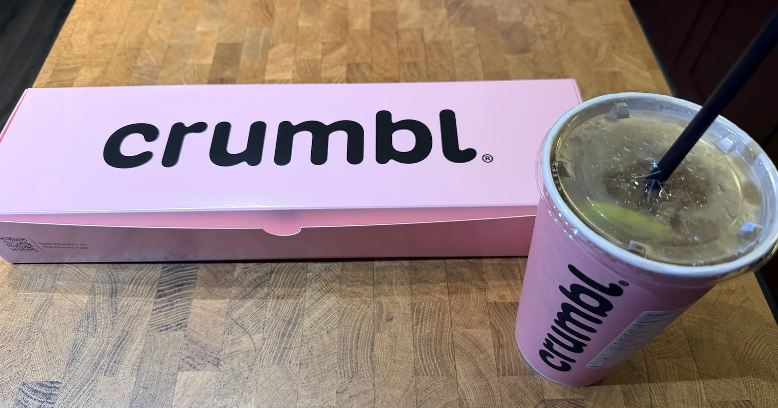 Hộp bánh quy màu hồng của Crumbl đặt cạnh ly dirty soda in logo Crumbl