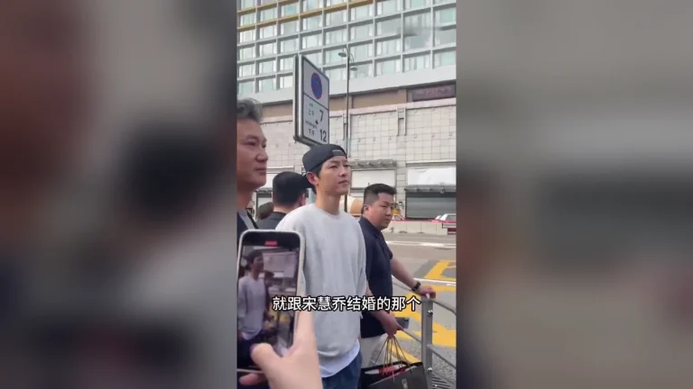 Song Joong Ki đội mũ lưỡi trai đứng trên vỉa hè, phía dưới là phụ đề tiếng Trung câu cô fan nhắc tới Song Hye Kyo
