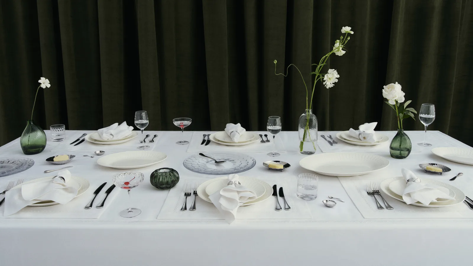 Bàn tiệc bày bộ sưu tập đồ bàn ăn Westwing x Victoria Beckham với đĩa sứ trắng, ly và bình hoa xanh